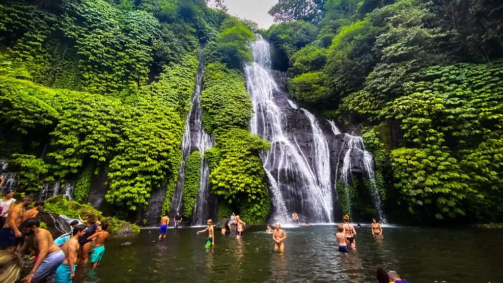 Tourists enjoying a swim in the clear natural pool at the base of Banyumala Twin Waterfalls