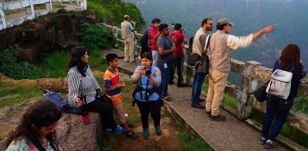 Tourists standing at a high-altitude viewpoint overlooking the vast Seven Sisters Waterfall valley