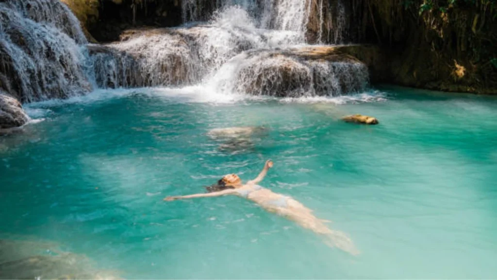 Tourists swimming in the clear blue natural pools of Kuang Si Waterfall