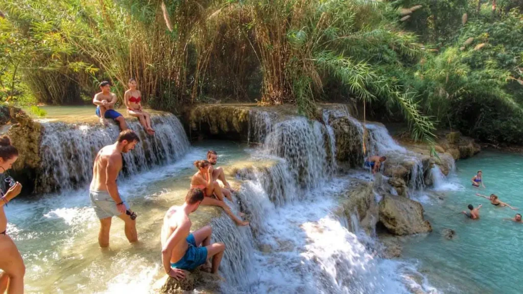 Tourists swimming in the clear blue natural pools of Kuang Si Waterfall